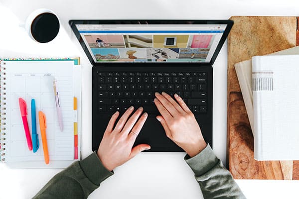 person working on a laptop at a desk with a planner